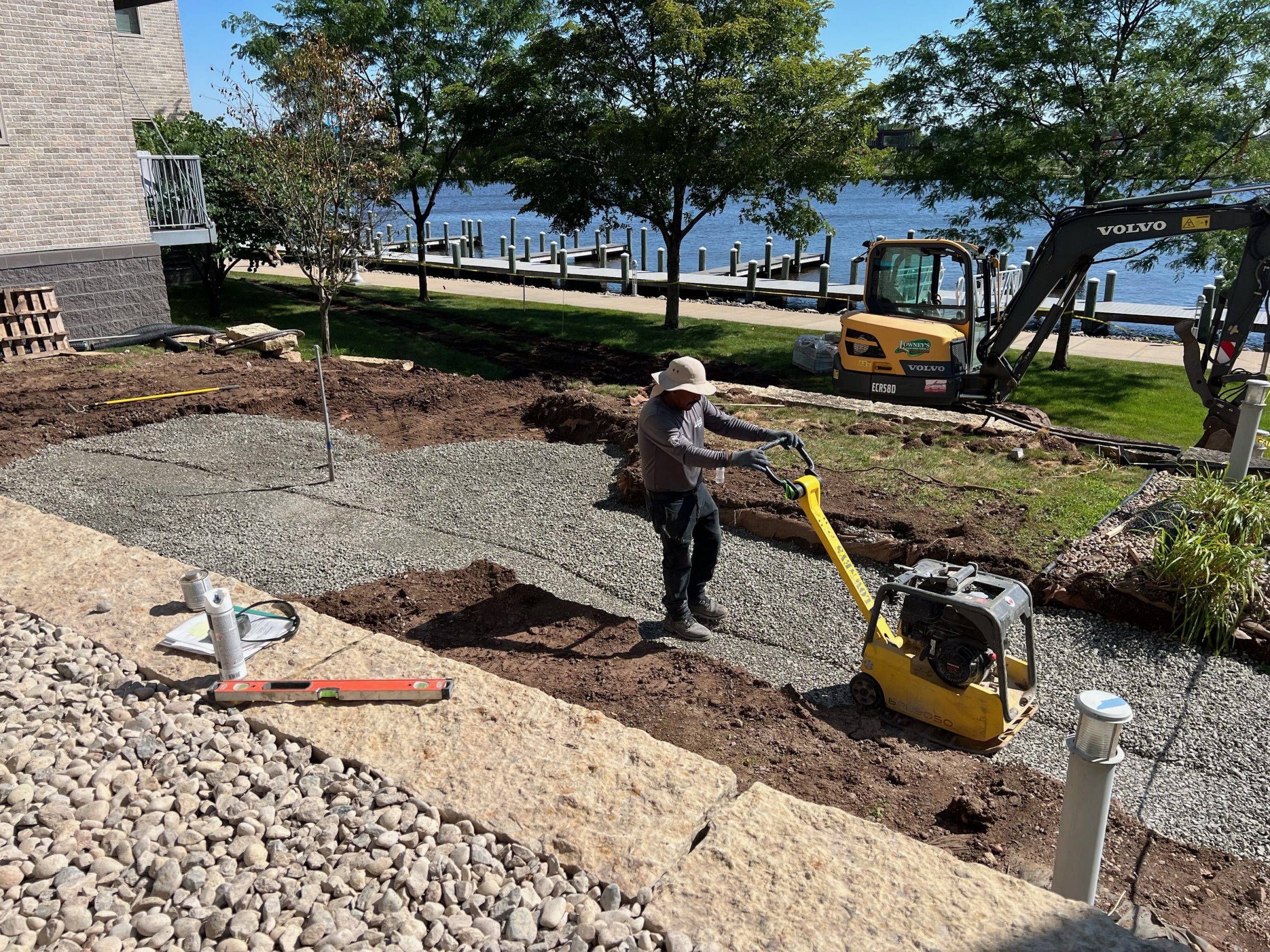 Worker compacting gravel near waterfront with excavator