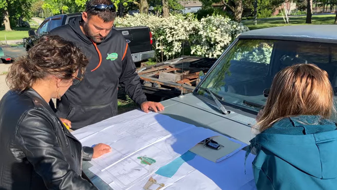 Three people reviewing blueprints on truck hood