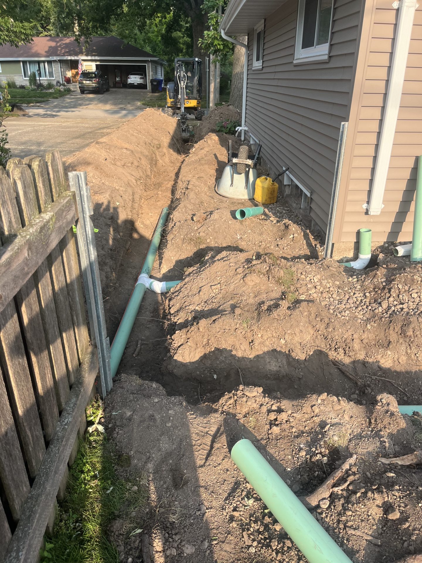 Trench with green pipes beside suburban house