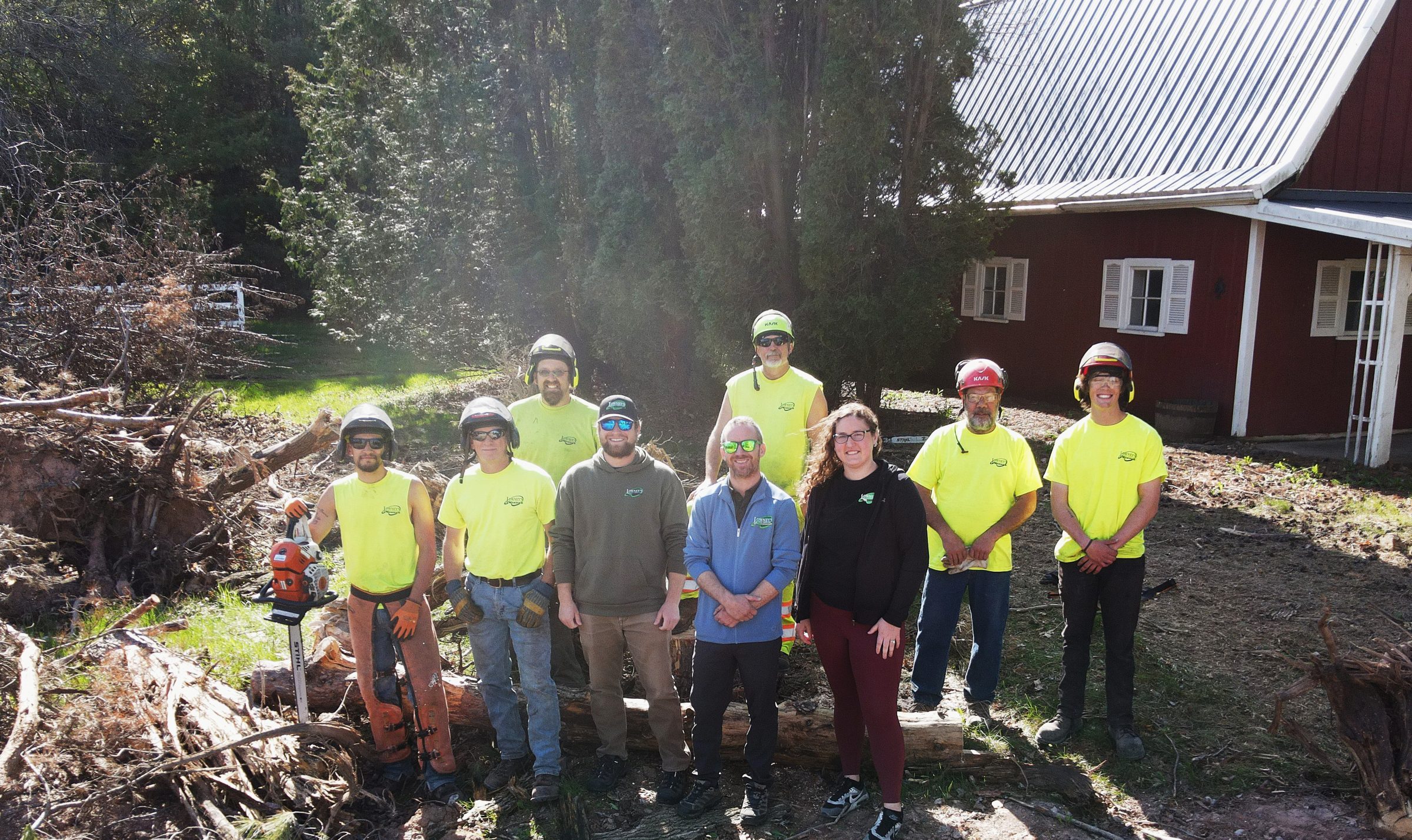 Tree service crew posing beside logs and barn