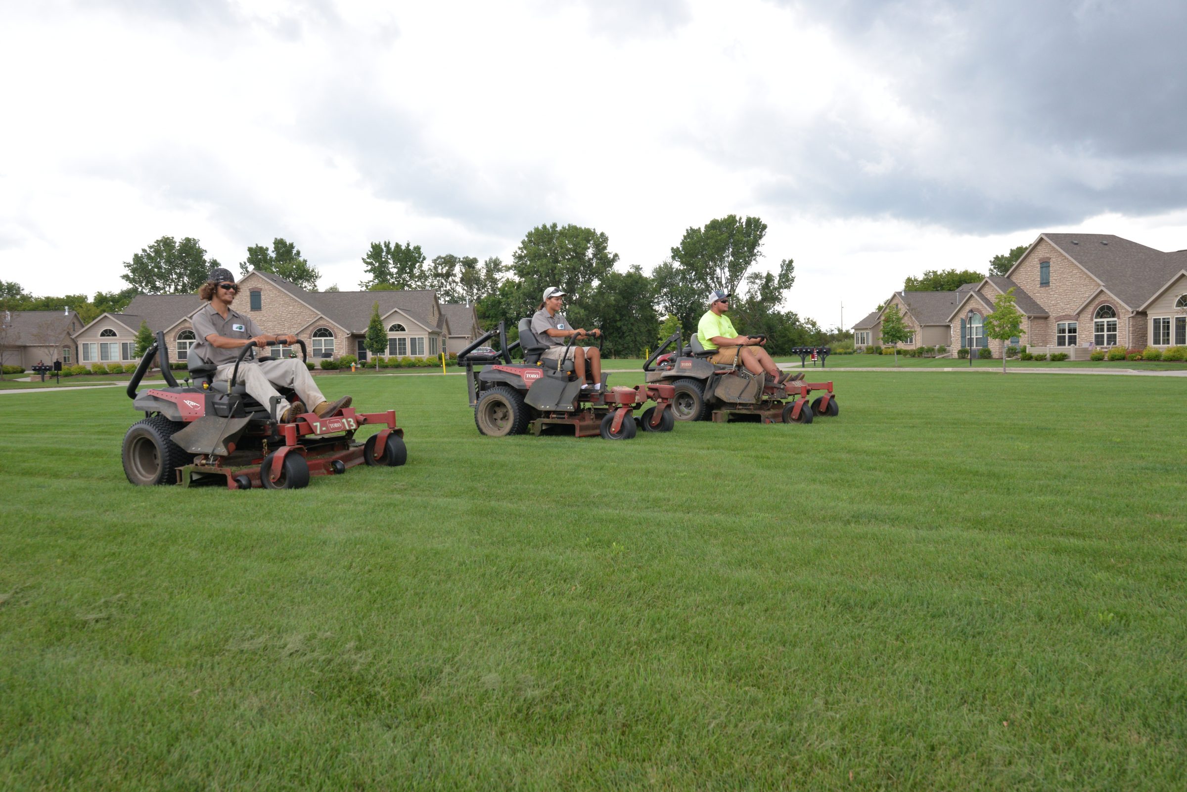 Three workers riding lawn mowers on green field