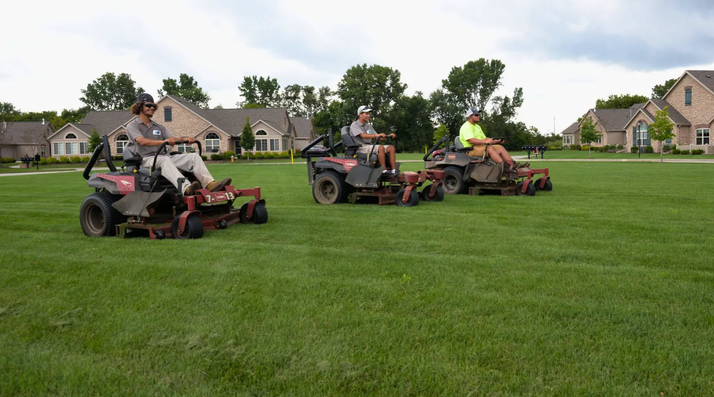 Three workers mowing lawn in suburban neighborhood