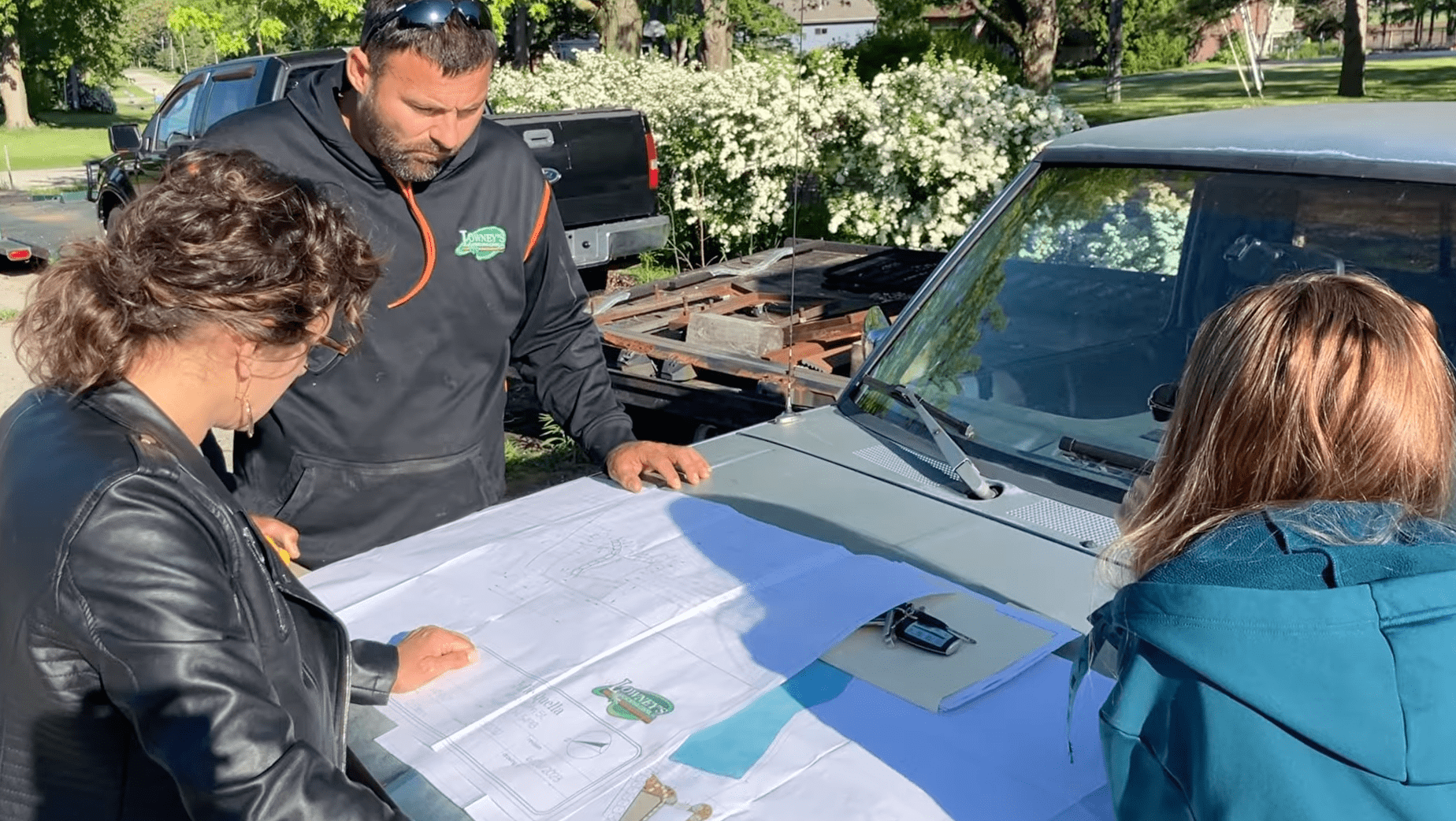 Three adults reviewing blueprints on car hood