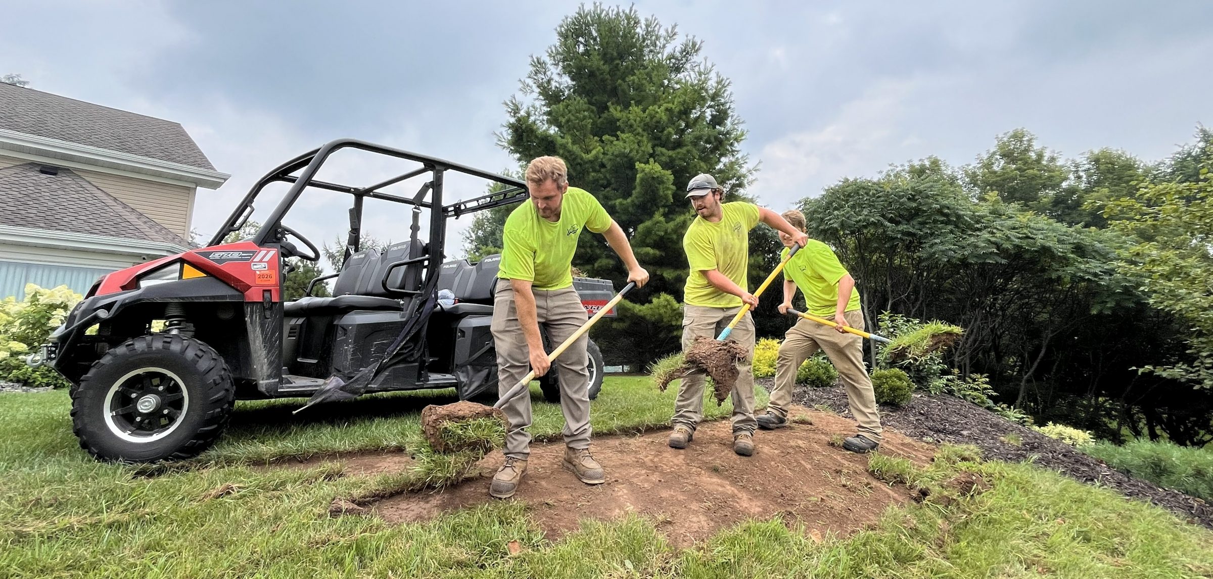 Landscapers removing sod with shovels beside utility vehicle