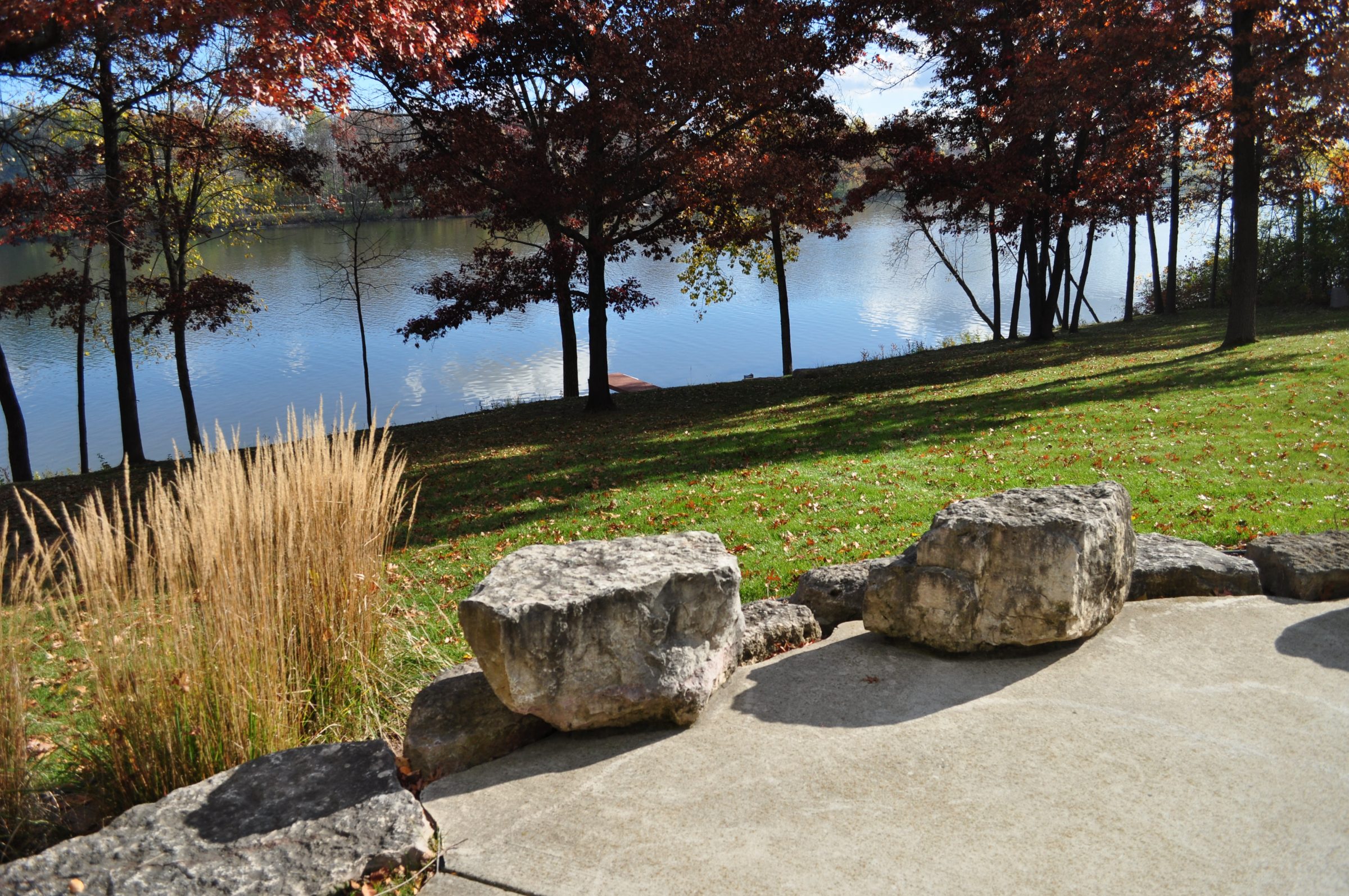 Autumn trees by calm lakeside with large rocks