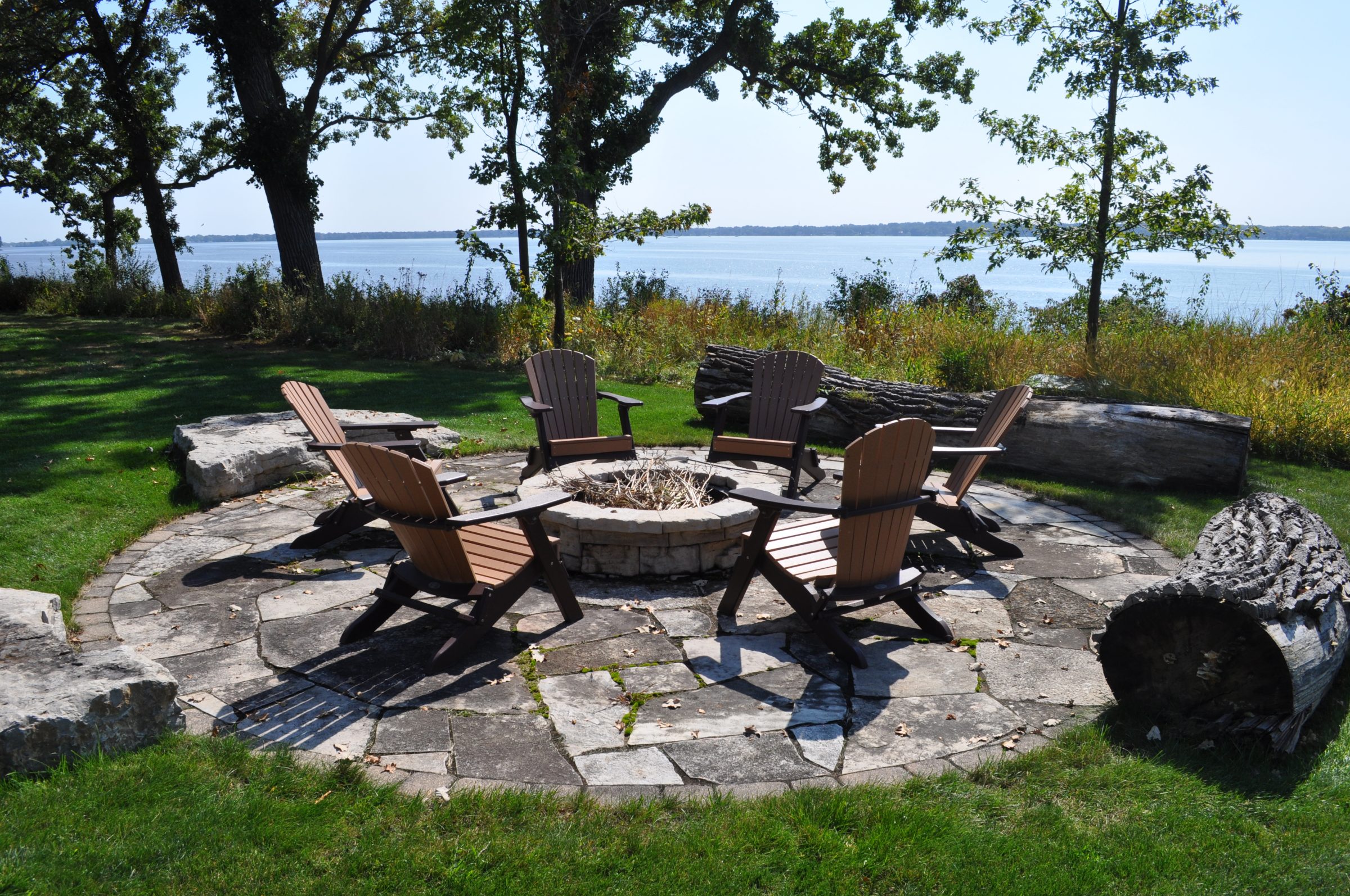 Adirondack chairs around fire pit by lakeside